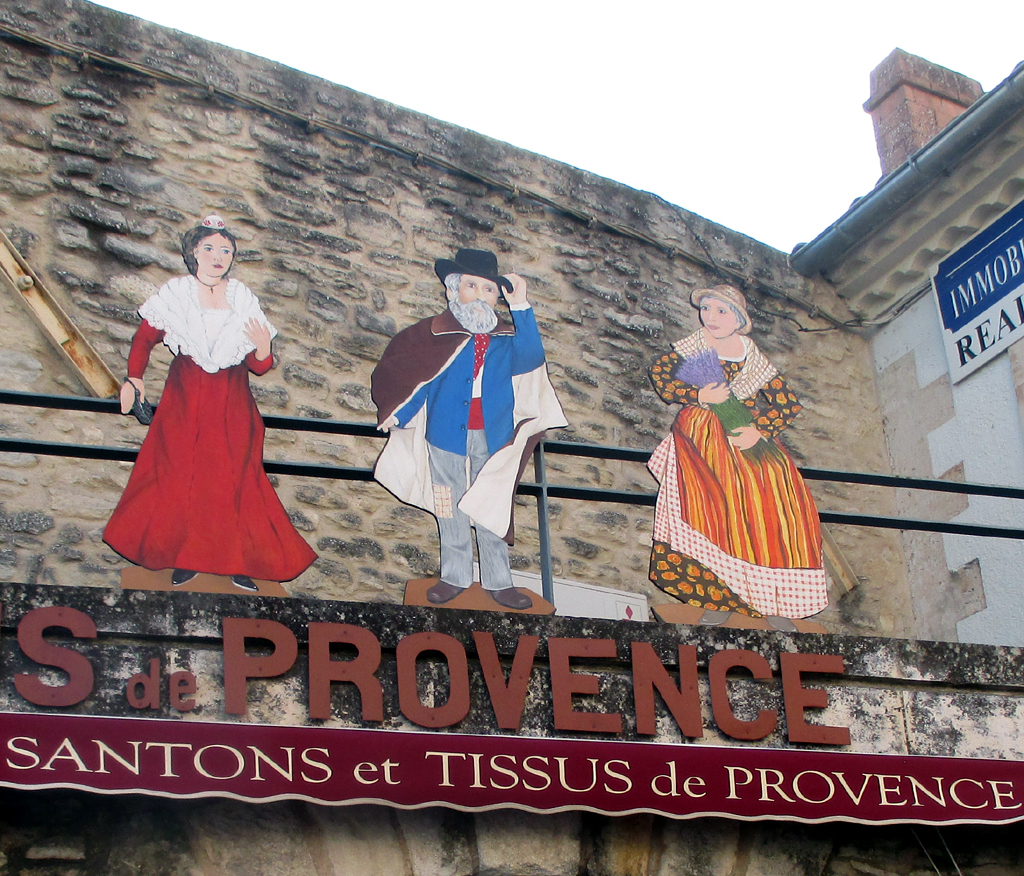 Werbung für provenzalische Krippenfiguren und Tücher über einem Geschäft in Gordes.