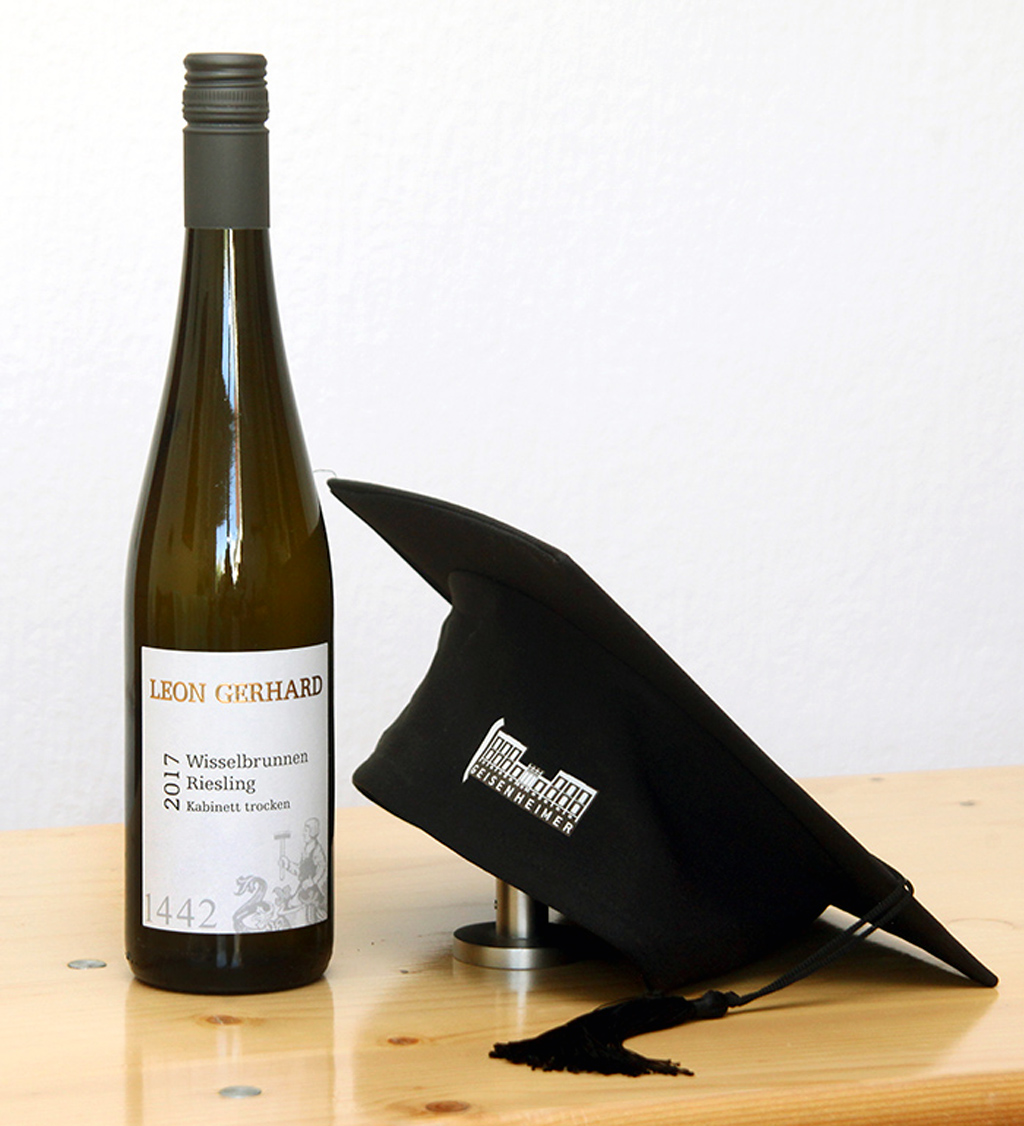 Michaela Gerhards Hut von der Absolventenfeier nach dem Weinbau-Studium in Geisenheim neben einem 2017er Wisselbrunnen Riesling Kabinett trocken vom Weingut Leon Gerhard.